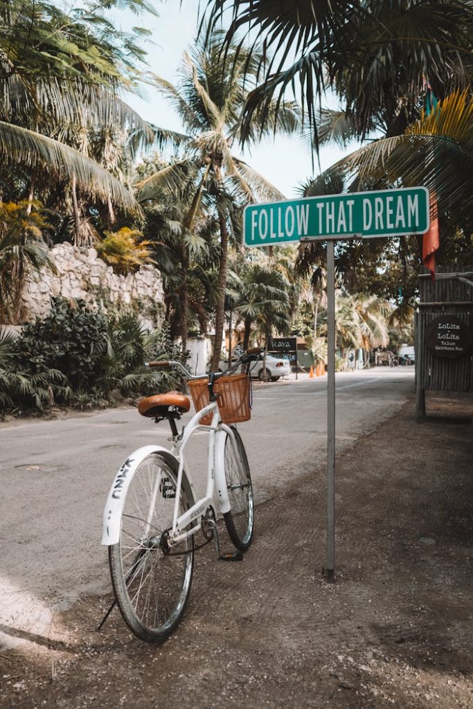 white-bicycle-parked-beside-green-signage-3727253 A bicycle near an inspirational sign Follow That Dream in Tulum, Mexico with palm trees around.